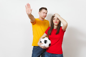 Sad upset young couple, woman, man, football fans in yellow red uniform with soccer ball cheer up team worries about losing team isolated on white background. Sport, family leisure, lifestyle concept.