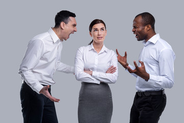 Teamwork. Pretty thoughtful dark-haired young woman thinking and standing between two angry men and men shouting at each other