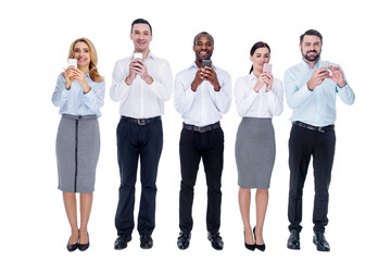 Obraz premium Inspired. Good-looking young exuberant colleagues standing in one line and using their phones and smiling
