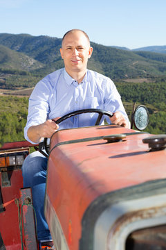 Confident  male owner of vineyard driving tractor outdoors in sunny day