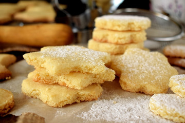 Shaped shortbread cookies covered with sugar powder surrounded by kitchen utensils