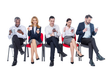 Relaxing. Attractive inspired stylish young co-workers smiling and drinking coffee and sitting on the chairs and using their phones