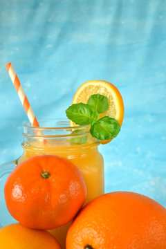 Orange, lemon, mandarin and yellow juice in a glass jar on blue background