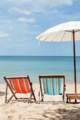 two beach lounge chairs under umbrella on beach.