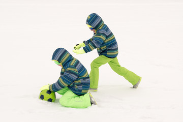 Fototapeta na wymiar A young lady in a blue ski suit plays football with children in the snow. Yellow sled, sunglasses, bright clothes. Girl happy outdoors. Fun winter vacation for the whole family. Green soccer ball