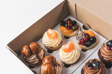 close up view of various types of cupcakes in cardboard box isolated on white