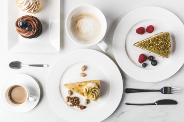 close up view of arrangement of pieces of various cakes on plates, cups of coffee and cupcakes isolated on white