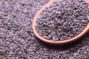 Black sesame in wooden spoon on sesame background.