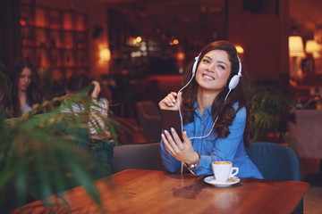 Young woman listening to music via headphones and smartphone in a cafe