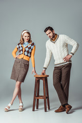 beautiful retro styled couple posing with wooden chair on grey