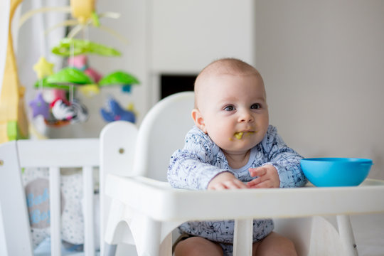 Cute little baby boy, eating mashed vegetables for lunch, mom feeding him