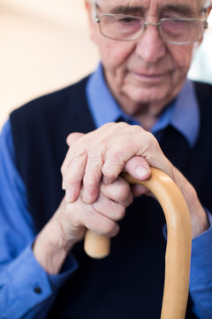Sad Senior Man Sitting In Chair Holding Walking Cane