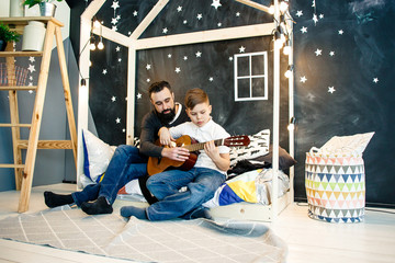 Bearded man teaching boy how to play on guitar