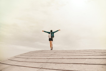 Feeling of Freedom. Young unidentified woman wearing casual clothes and backpack raises hands up...