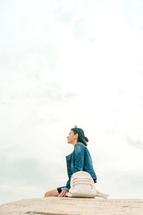 Alone with the elements. Unknown young woman tourist with backpack sits on concrete hill and admires deserted view