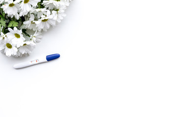 Joy of long-awaited pregnancy. Pregnancy test with two stripes near flowers on white background top view copy space