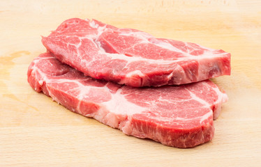 Two raw pork neck meat cuts isolated on wood background fresh slices without bone .