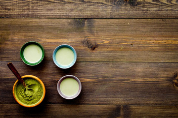 Brew matcha tea. Bowl with powder and cups with beverage on dark wooden background top view copy space
