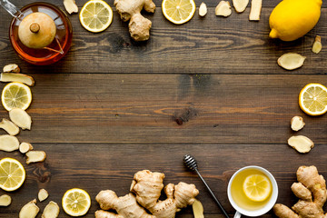 Tea for cure colds. Cup, teapot, ginger root and lemon on dark wooden background top view copy space