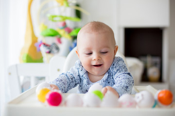 Cute little toddler boy, playing with plastic eggs, sitting in a white chair in a sunny living room