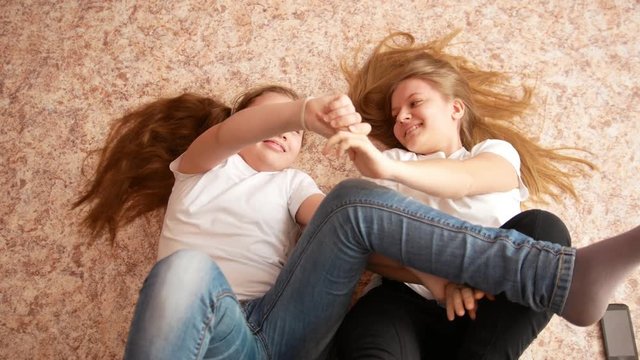 Two teenagers sisters girls lying on the floor - playing and have fun