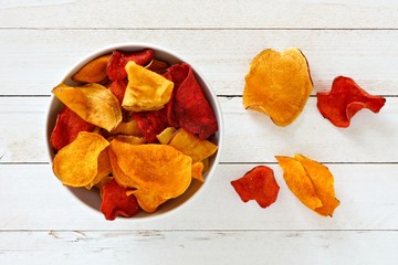 Bowl of mixed healthy vegetable chips. Top view, still life on a white wood background.