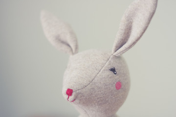 Cute toy bunny close up with natural background. Single object, light beige. Shallow depth of field. Easter bunny. Minimalistic. Matte vintage filter.
