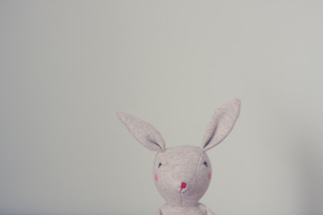 Cute toy bunny close up with natural background. Single object, light beige. Shallow depth of field. Easter bunny. Minimalistic. Matte vintage filter.