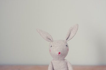 Cute toy bunny close up with natural background. Single object, light beige. Shallow depth of field. Easter bunny. Minimalistic. Matte vintage filter.
