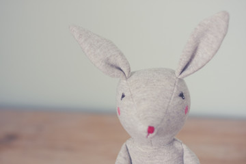 Cute toy bunny close up with natural background. Single object, light beige. Shallow depth of field. Easter bunny. Minimalistic. Matte vintage filter.