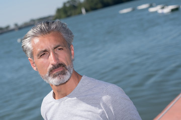 handsome man posing in front of sailing boats and lake