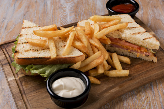 grilled sandwich with tomato ham cheese and french fries on a board with sauce
