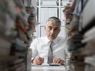 Frustrated businessman and piles of paperwork