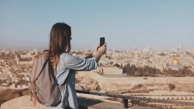 Tourist girl takes photos of old town Jerusalem. Girl with backpack walks to skydeck edge. Capturing moments. Israel 4K.