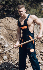 Muscular builder on sunny day works at construction site.