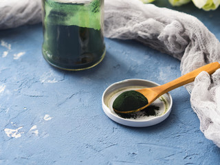 Spirulina powder on a wooden spoon over blue background