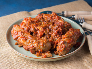 Sausages and pork pullet cooked in traditional Italian tomato ragu sauce. Dish on burlap with cutlery.