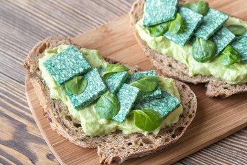Slices of toasted bread with avocado paste and basil cheese
