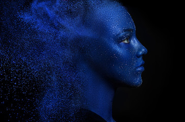 beautiful girl face painted with blue paint with glitter. The effect of dispersed particles. Flying blue powder.