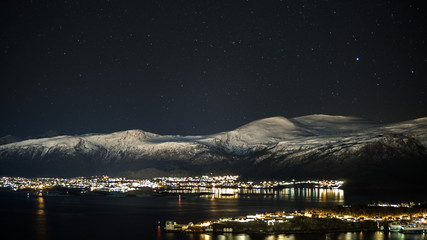 Nightshot of snow covered mountains with fjords and city. Aalesund in Norway. Beautiful destinations in Europe.