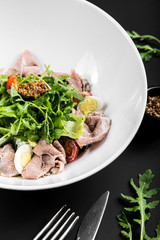 salad with roast beef, arugula, cherry tomatoes, egg and grain mustard on a black background. close up