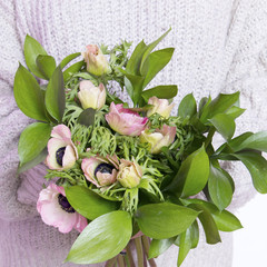 girl in white wool sweater holds a wedding bouquet of anemones and Ruscus on the white background