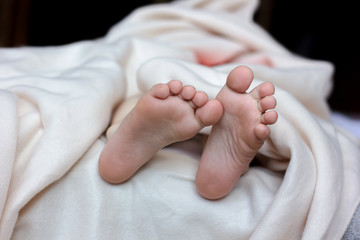 Kid laying in the bed and foot with toes and heels on white blanket.