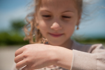 cute small girl holding a butterfly on her hand and looking at her