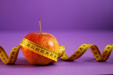 An apple wrapped with a measuring tape, selective focus, violet background, free copy space