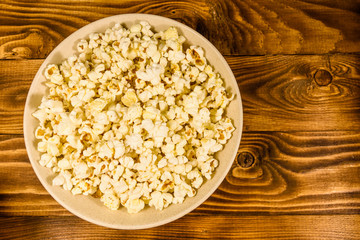Ceramic plate with popcorn on wooden table. Top view