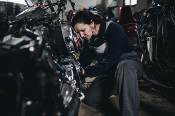 Strong and worthy woman doing hard job in car and motorcycle repair shop.