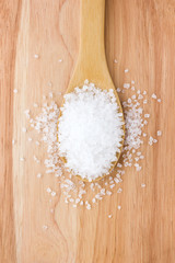 Sea salt in a wooden spoon. Large sea salt sprinkled on the table.
