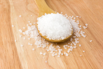 Sea salt in a wooden spoon. Large sea salt sprinkled on the table.