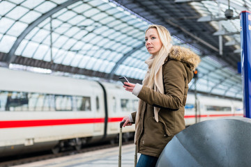 Frau im Bahnhof nutzt die Fahrplan App während der Zug einfährt - obrazy, fototapety, plakaty